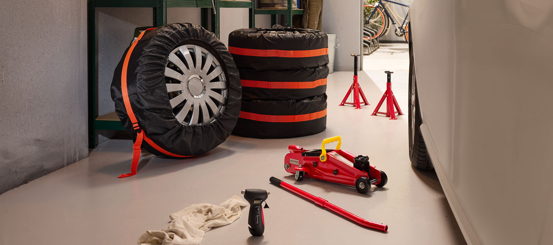 Auton renkaat suojuksineen, tunkki ja pukit autotallissa.