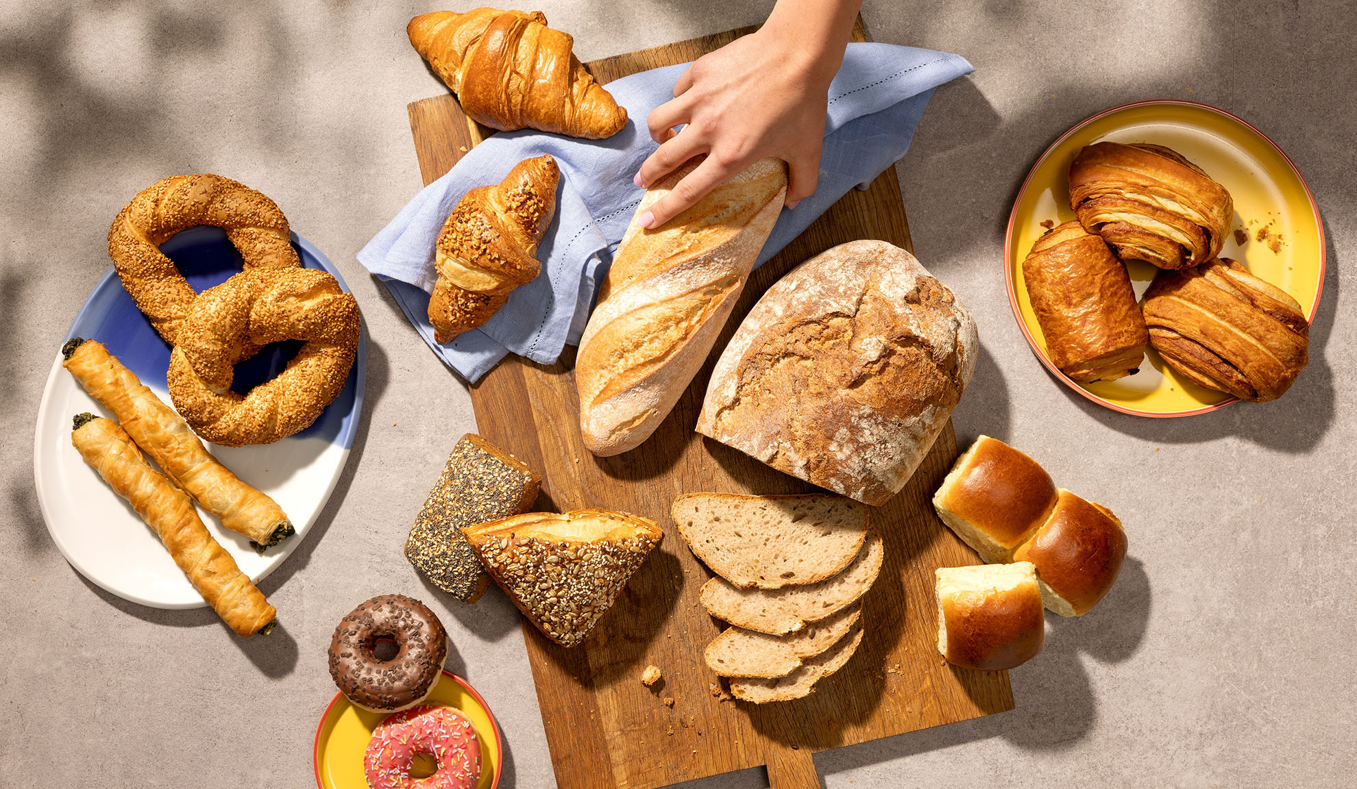 Valikoima tuoreita leivonnaisia, kuten leipää, croissanteja, leivoksia ja munkkeja pöydällä.