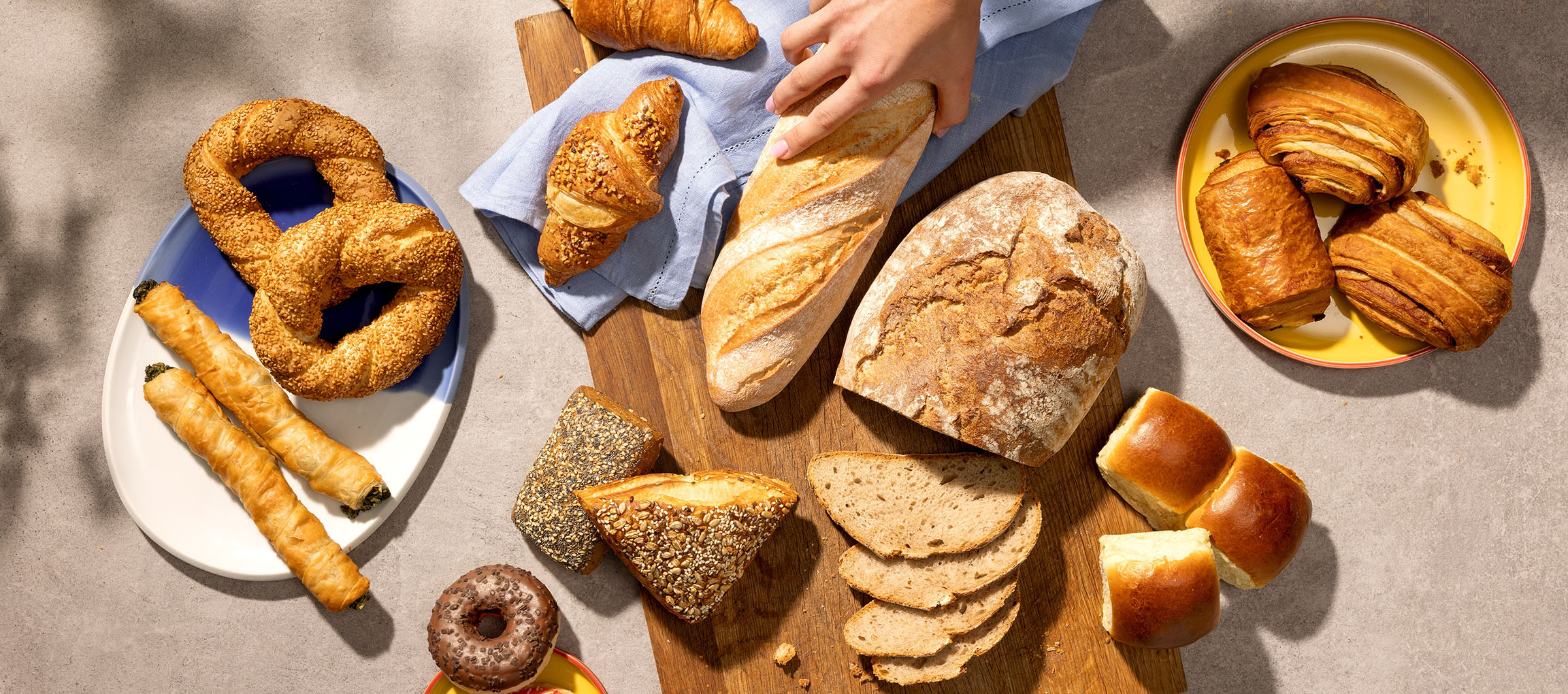 Valikoima leivonnaisia ja leipää, mukaan lukien rinkeleitä, croissanteja ja patonkeja, pöydällä.