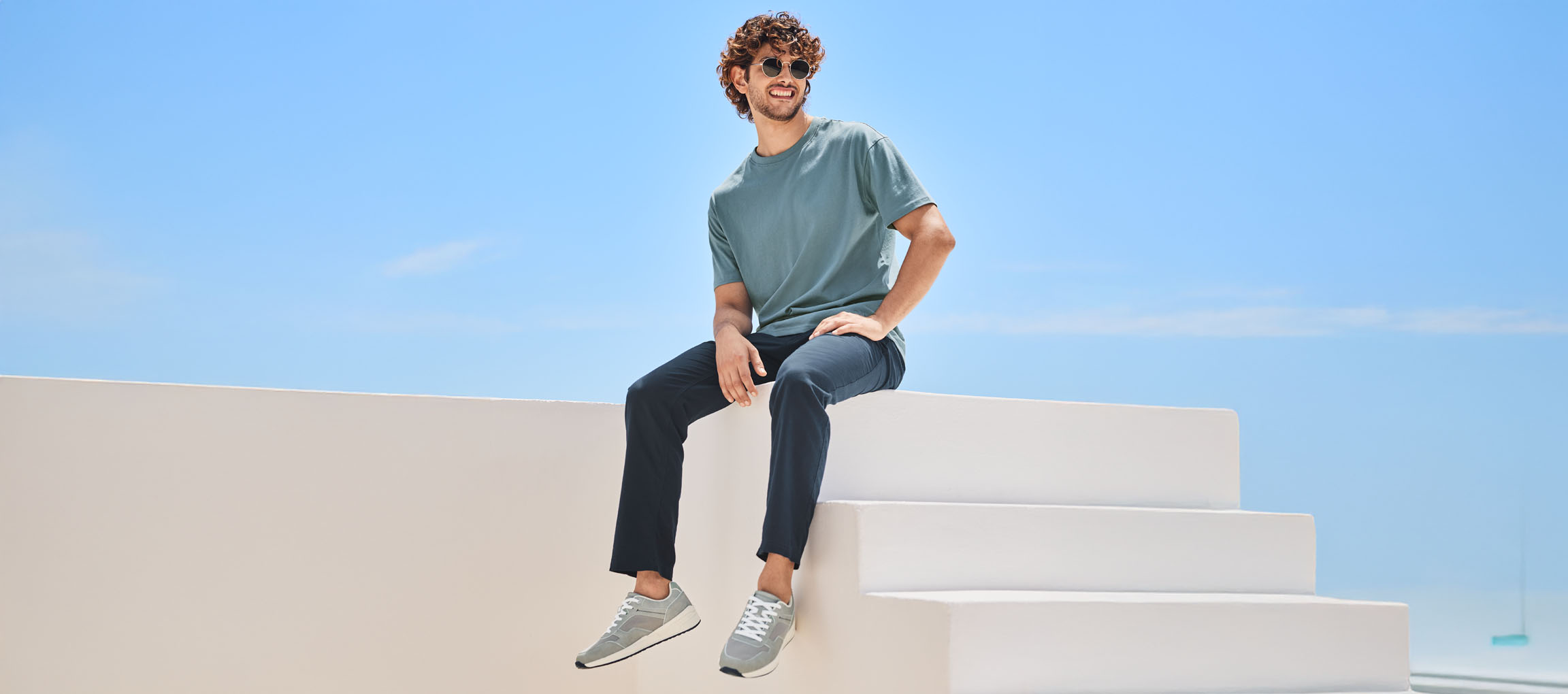 Mies t-paidassa, housuissa ja New Balance -lenkkareissa istuu valkoisilla portailla.