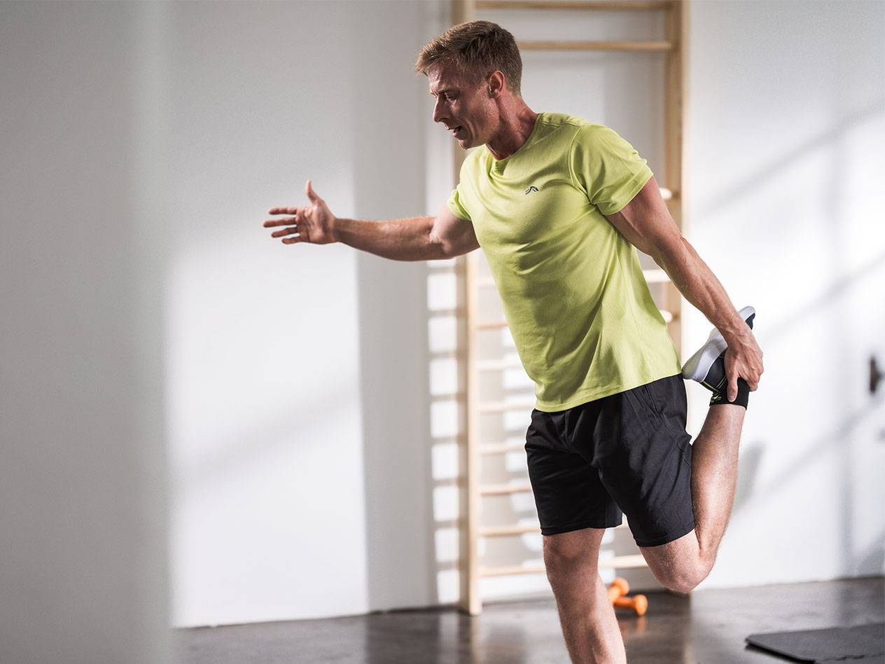 Mies venyttelee mustissa shortseissa ja limenvihreässä t-paidassa kuntosalilla.