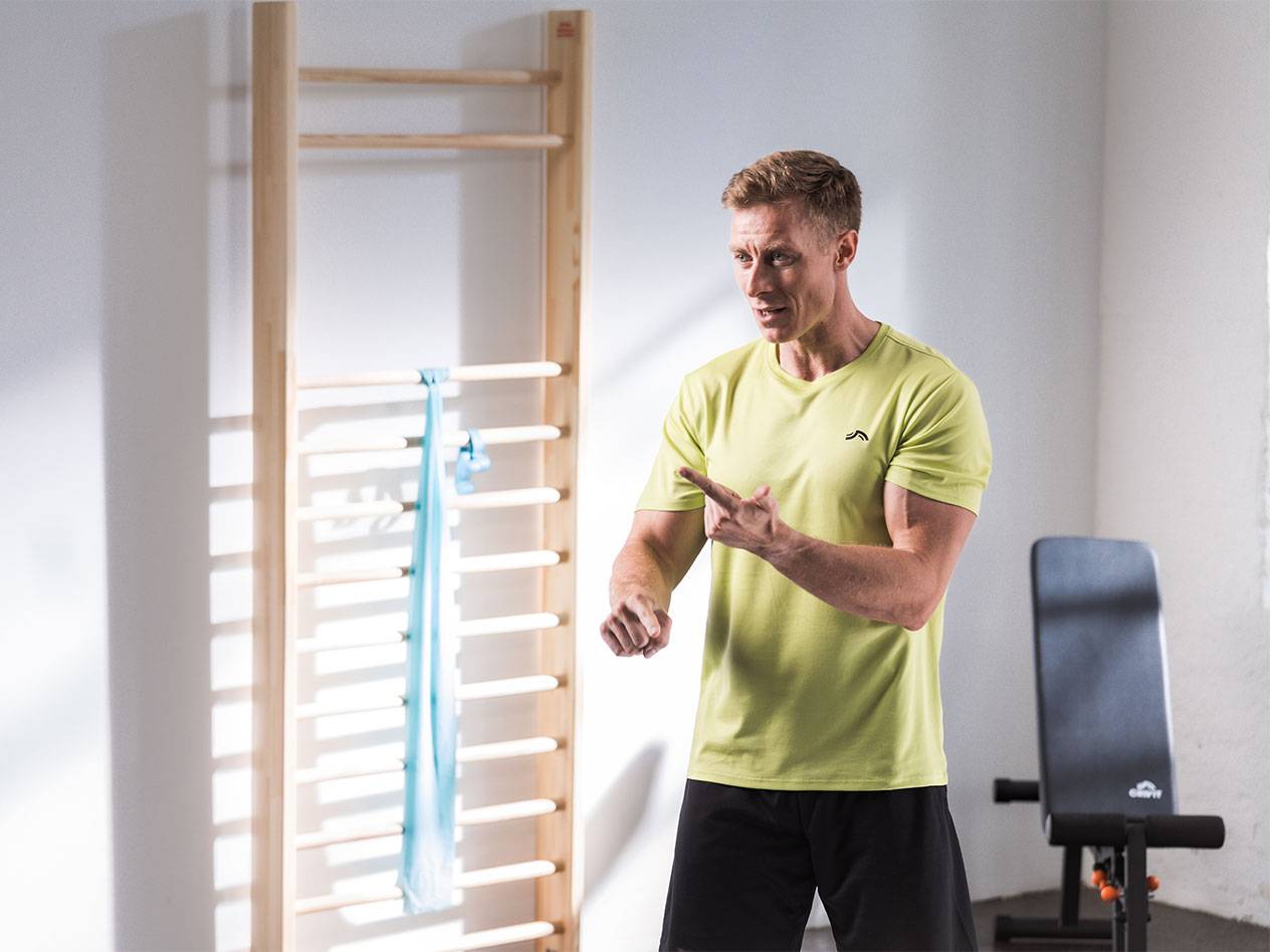 Mies urheiluvaatteissa seisoo puolapuiden edessä vastuskuminauhan kanssa.