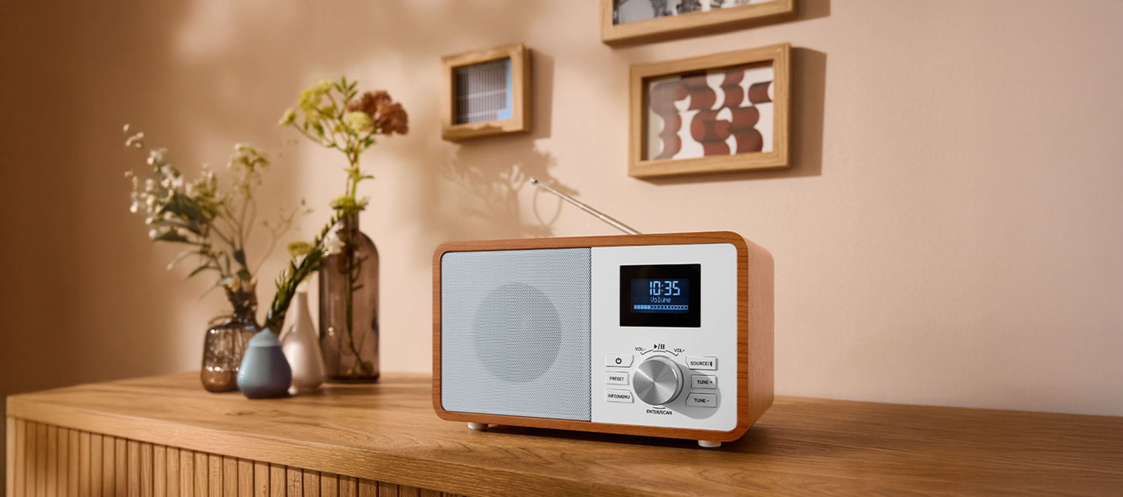 Puinen digitaalinen radio lipaston päällä, maljakoita ja tauluja seinällä.