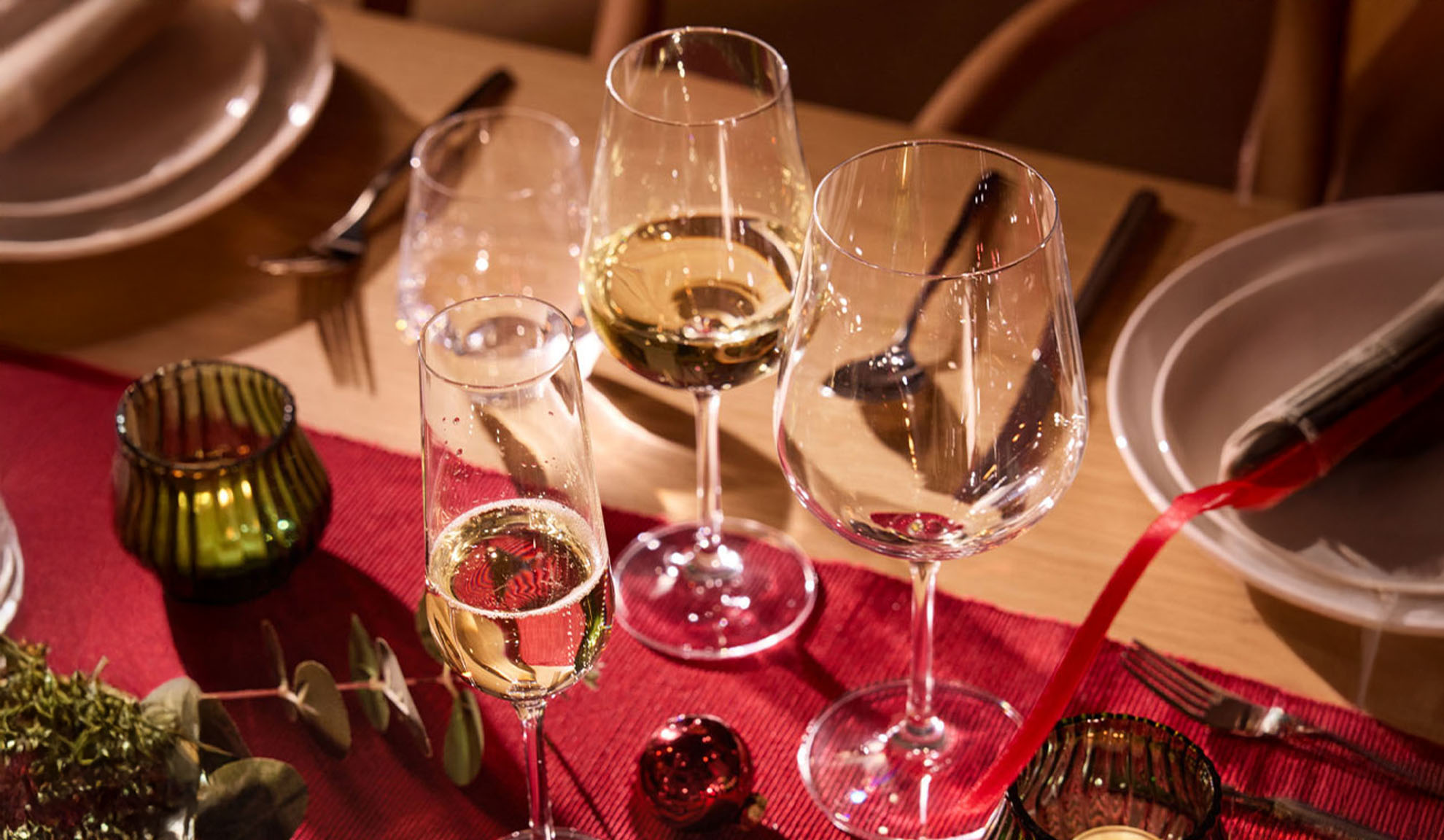 Juhlavasti katettu pöytä viinilaseilla, samppanjalasilla ja joulukoristeilla.