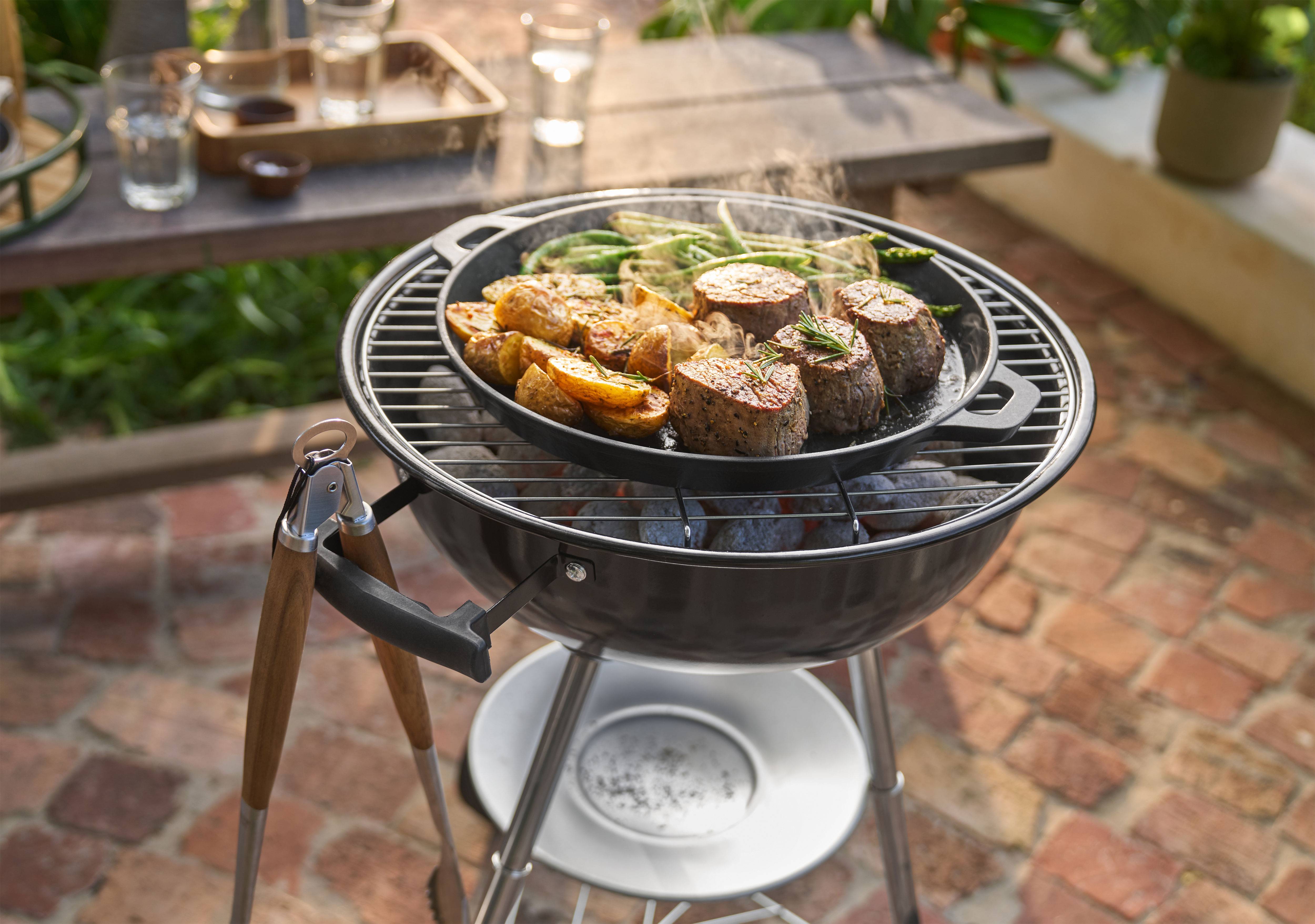 Grilli, jossa lihaa, perunoita ja vihreitä papuja kypsennetään pannulla ulkona.