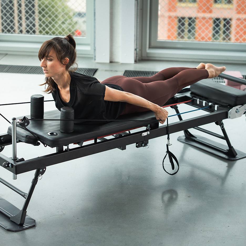 Nainen harjoittelee Pilates-laitteella vastuskuminauhojen kanssa.