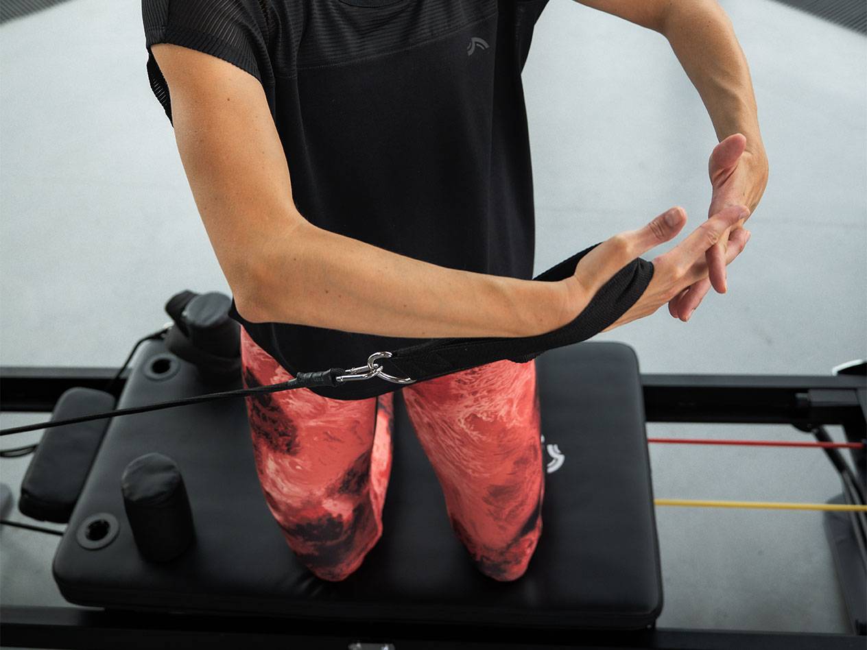 Nainen harjoittelee vastuskuminauhoilla Pilates-laitteella.