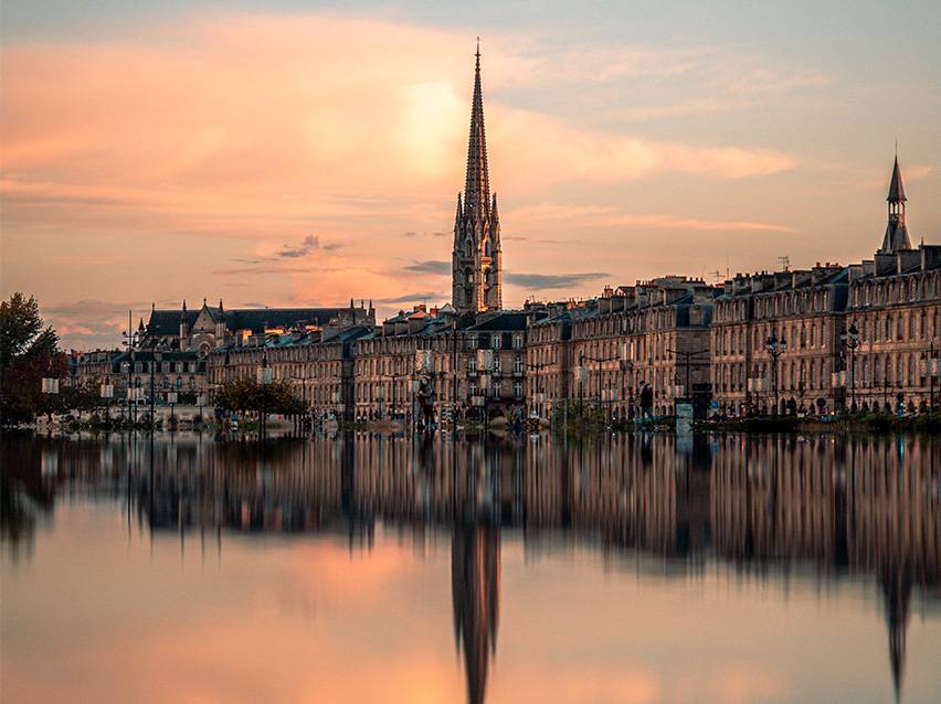 Bordeaux'n kaupunkikuva auringonlaskussa kirkon ja sen heijastuksen kanssa vedessä.
