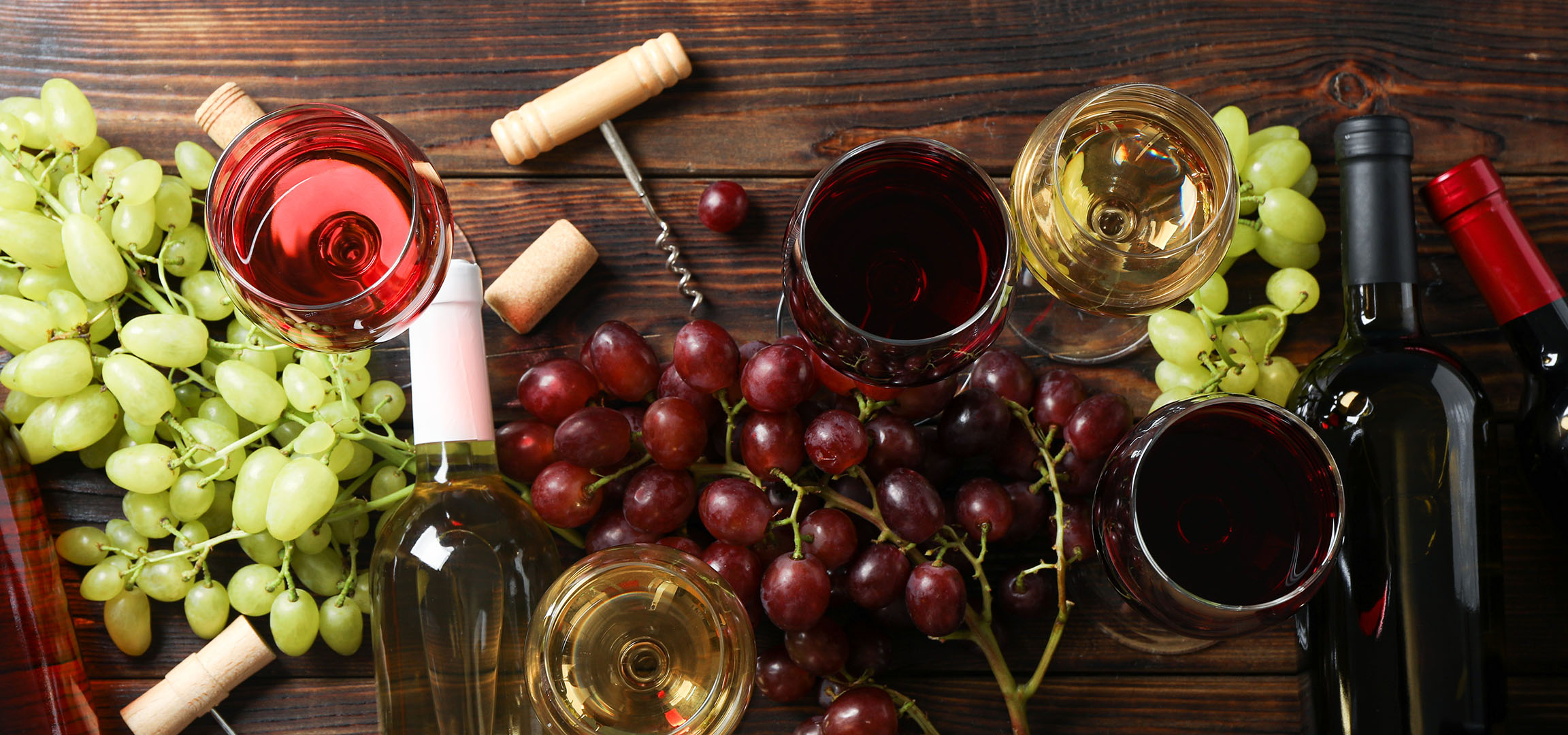 Erilaisia viinejä, rypäleitä ja viinitarvikkeita puupöydällä.