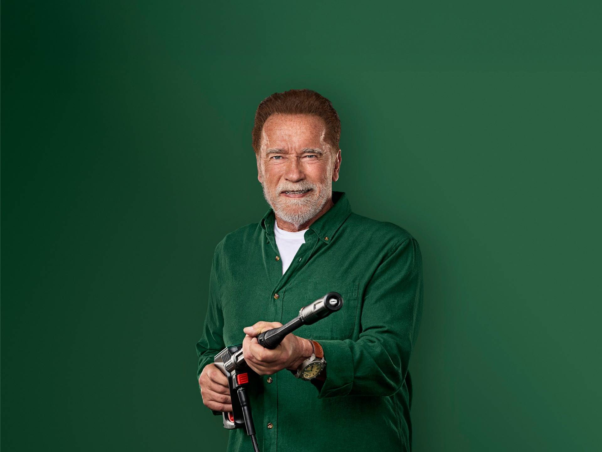 Arnold Schwarzenegger hymyilee pitäen painepesurin pistoolia.