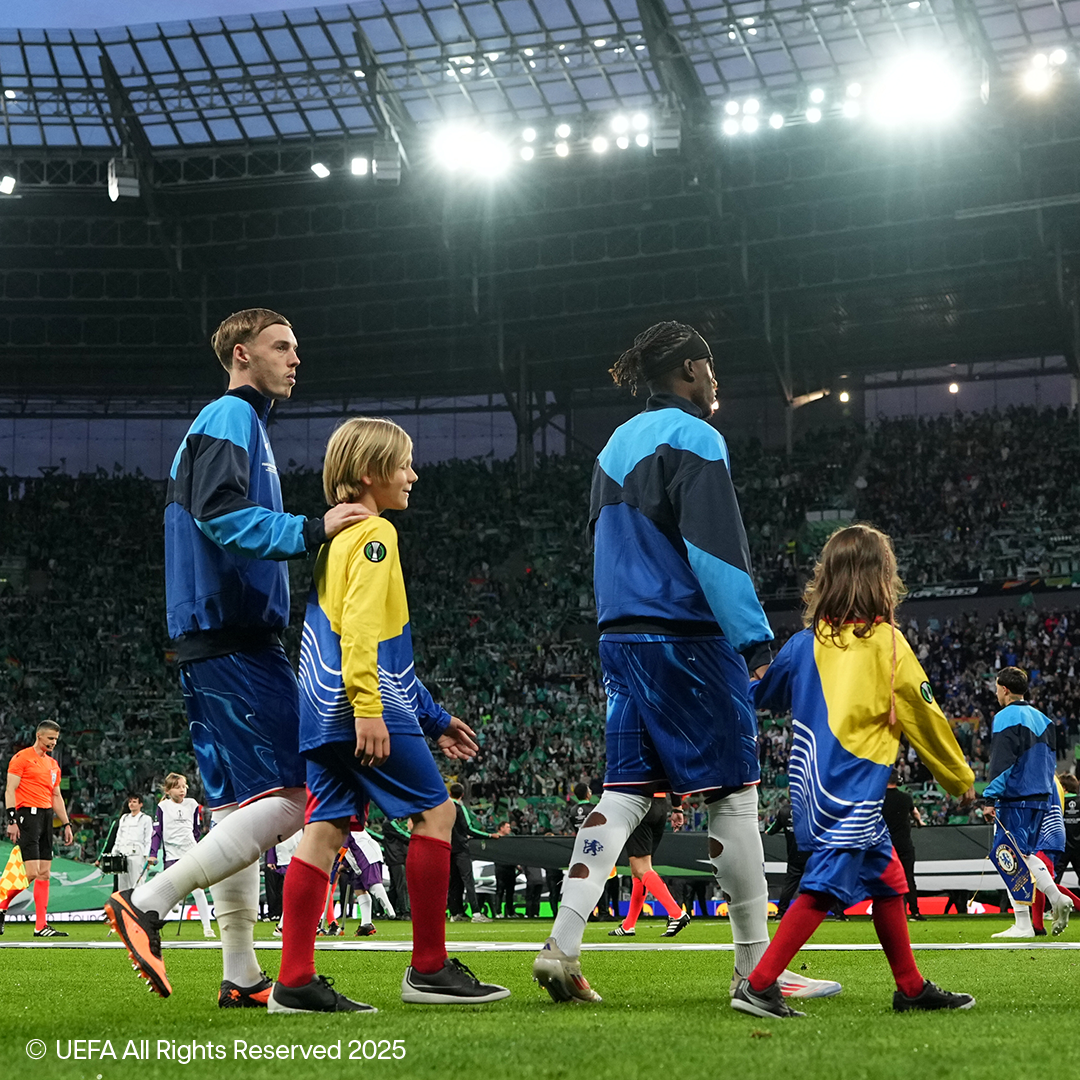 Jalkapalloilijat ja lapset kävelevät täyden stadionin kentällä.