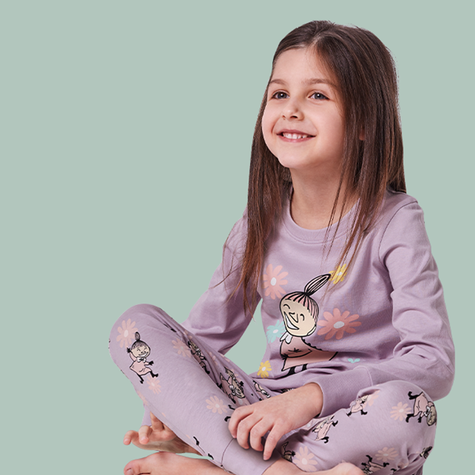 Tyttö istuu jalat ristissä yllään Muumi-aiheiset pyjamat, joissa on Pikku Myy ja kukkia.