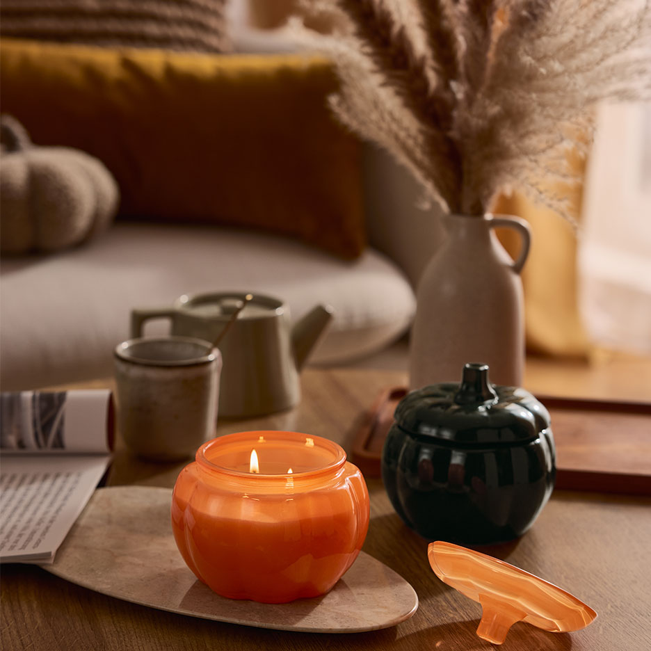 Kurpitsanmuotoinen kynttilä ja astia sohvapöydällä syksyisellä sisustuksella.