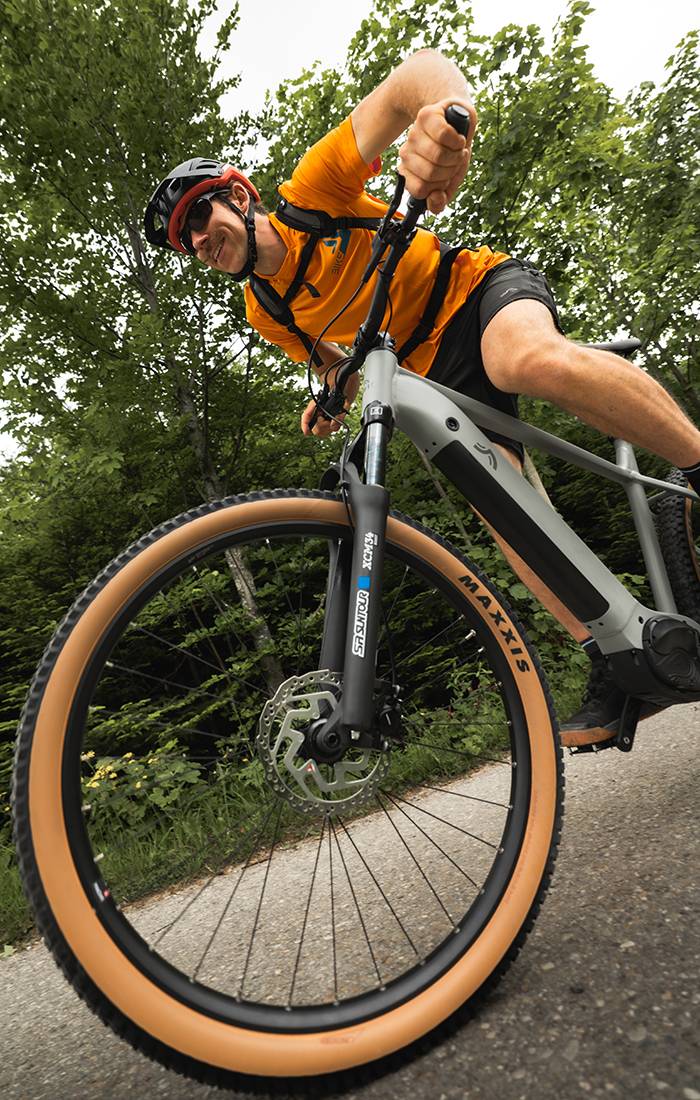 Mies ajaa harmaalla Maxxis-sähköpyörällä metsässä.