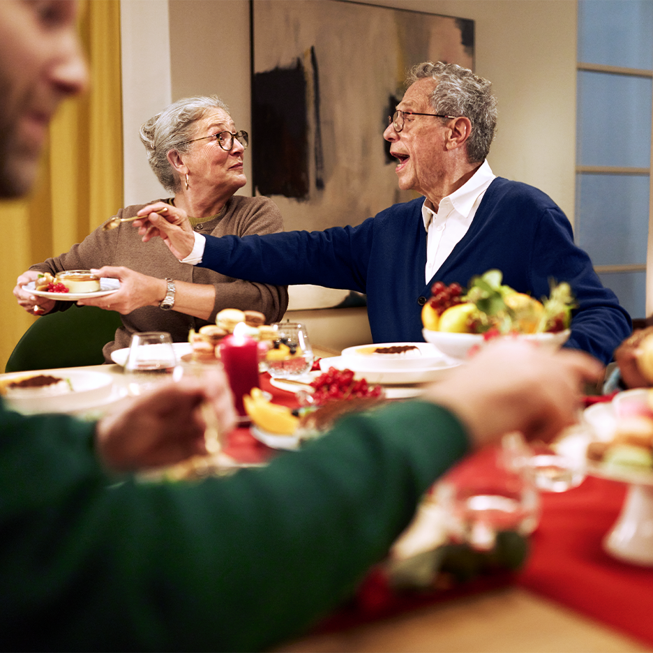 Iäkäs pariskunta nauttii jälkiruoista ja hedelmistä juhlallisesti katetussa pöydässä.