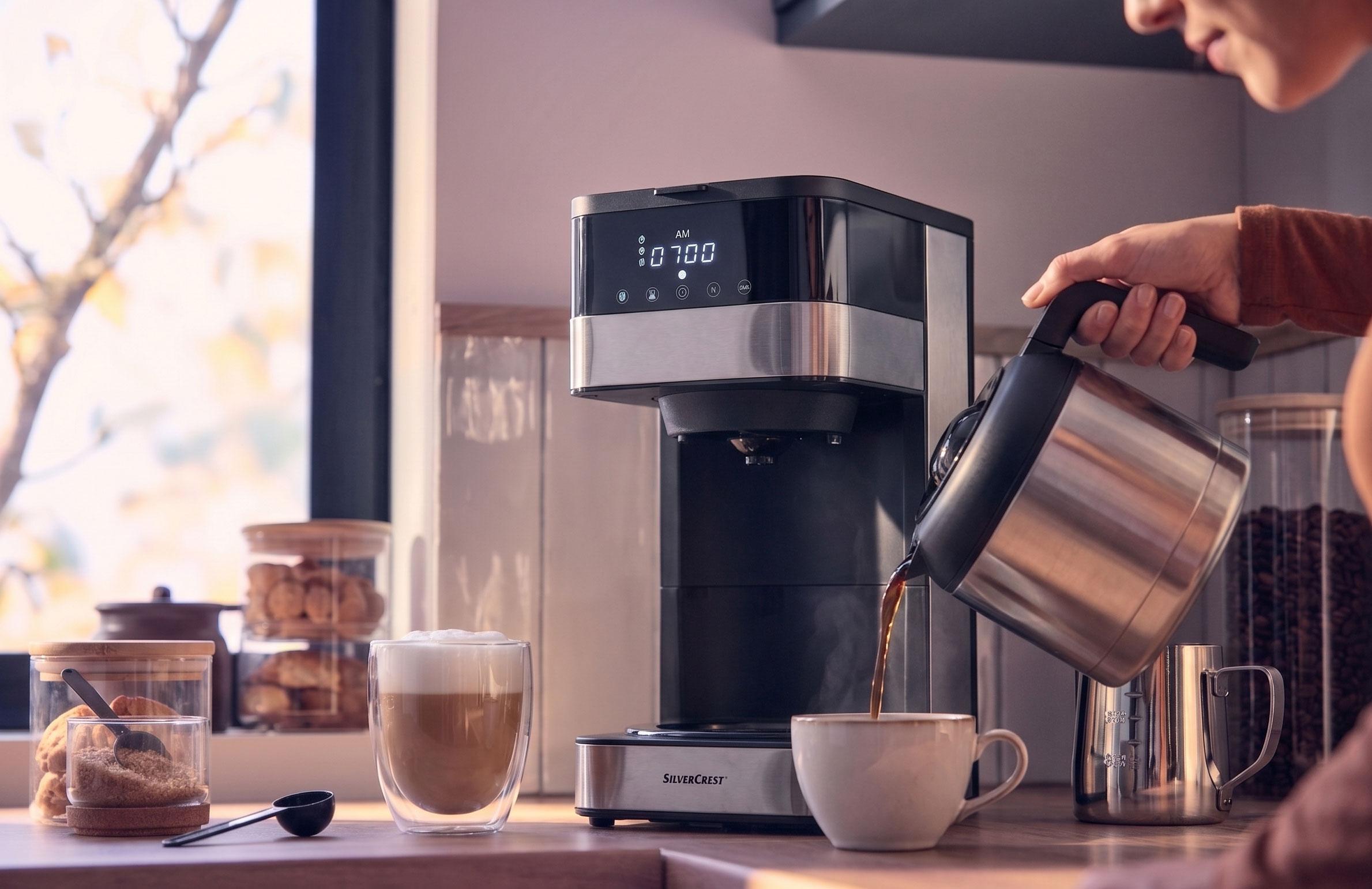 Kahvinkeitin kaataa kahvia kuppiin, jossa on latte ja keksejä tiskillä.