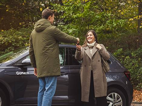 Mies ojentaa auton avaimia hymyilevälle naiselle auton vieressä.