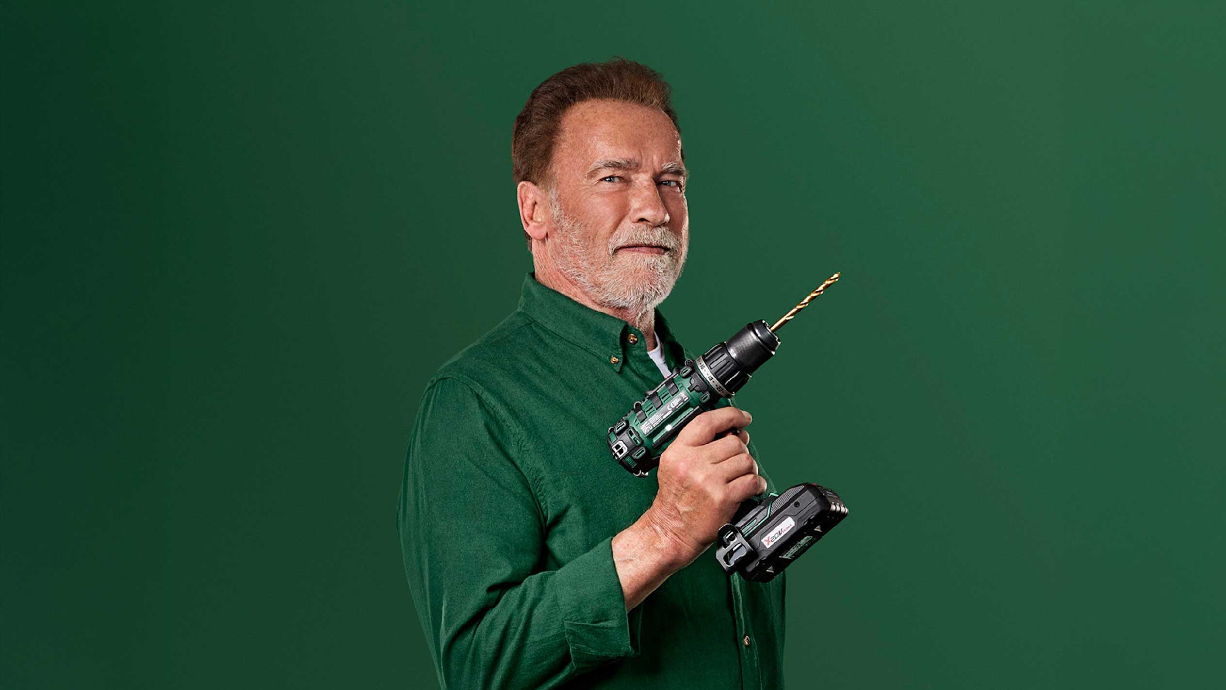 Arnold Schwarzenegger pitää vihreää akkuporakonetta kultaisella poranterällä.