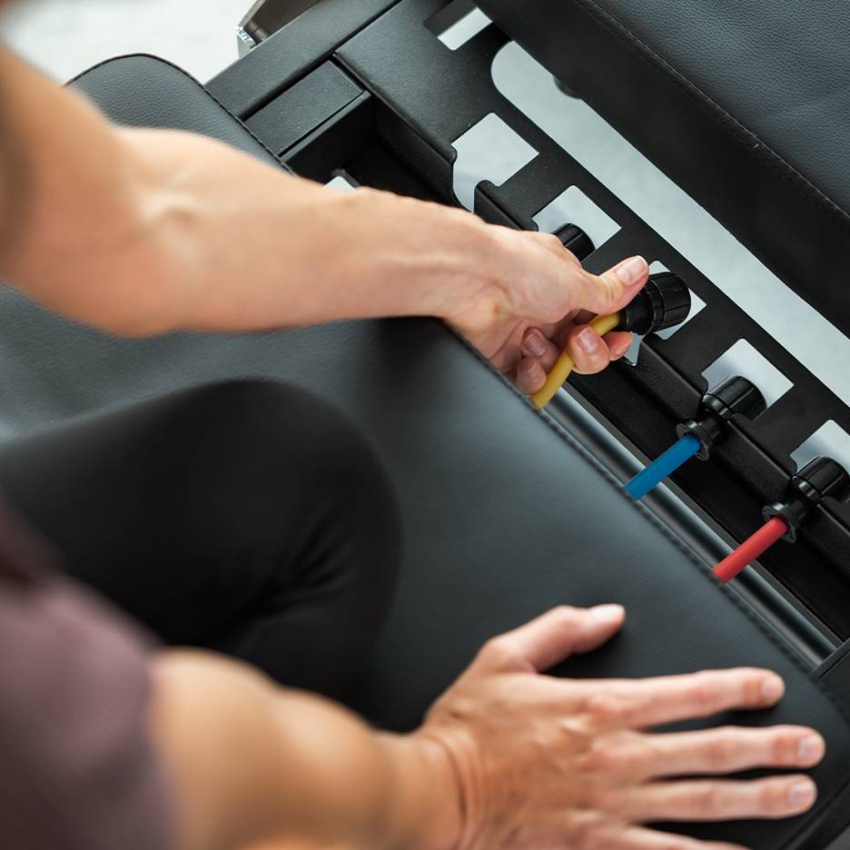 Henkilö säätää vastuskuminauhoja harjoituspenkillä.