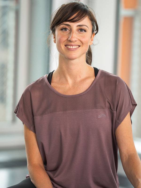 Hymyilevä nainen yllään lyhythihainen violetti urheilutoppi.