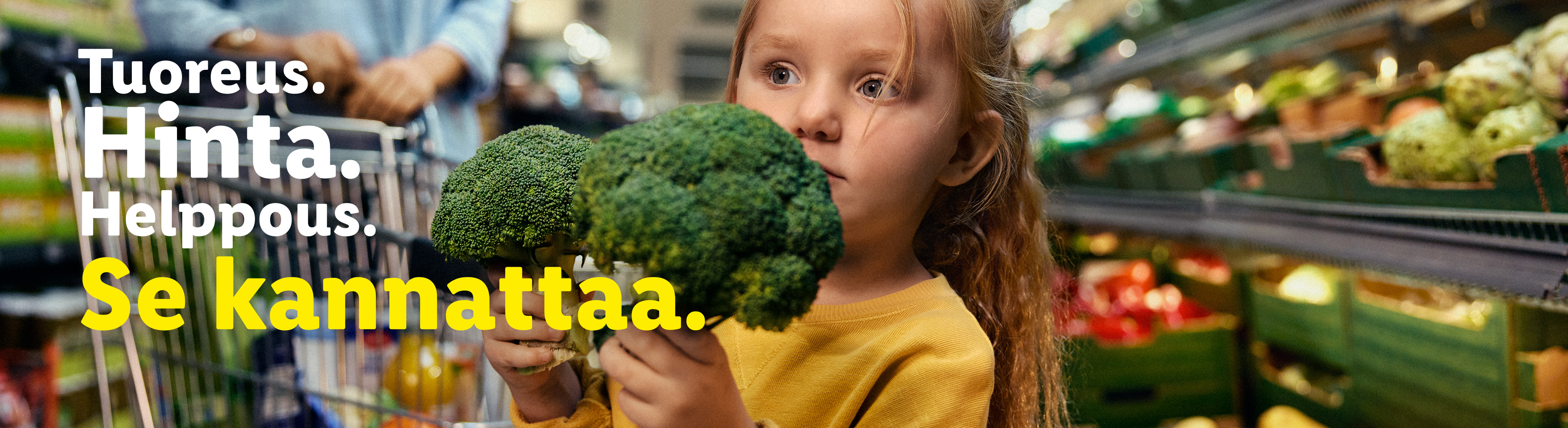 Lapsi pitelee parsakaalia ruokakaupassa. Teksti: Tuoreus. Hinta. Helppous. Se kannattaa.