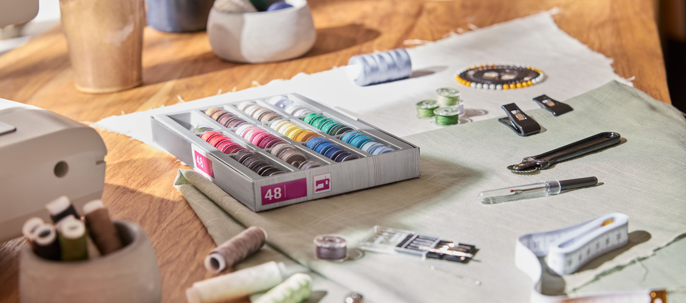 Ompelutarvikkeita puupöydällä, mukaan lukien lankajärjestelijä 48 puolalla, kangasta ja erilaisia työkaluja.