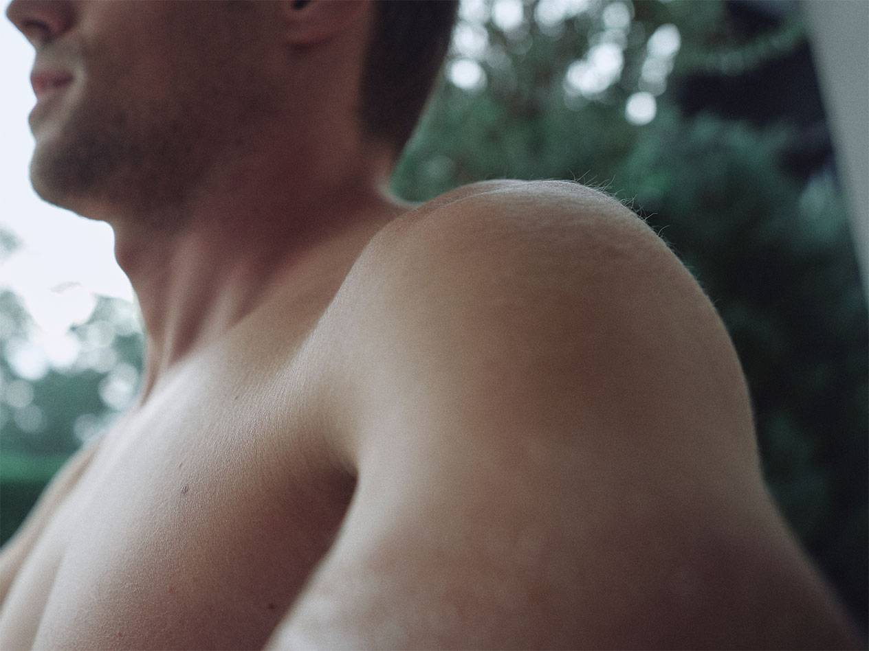 Lähikuva miehen olkapäästä ja kaulasta, sumea vihreä tausta.
