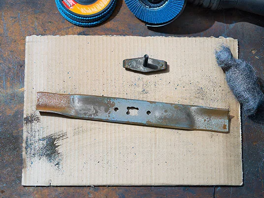 Ruosteinen ruohonleikkurin terä pahvilla hiomalaikkojen ja teräsvillan kanssa.