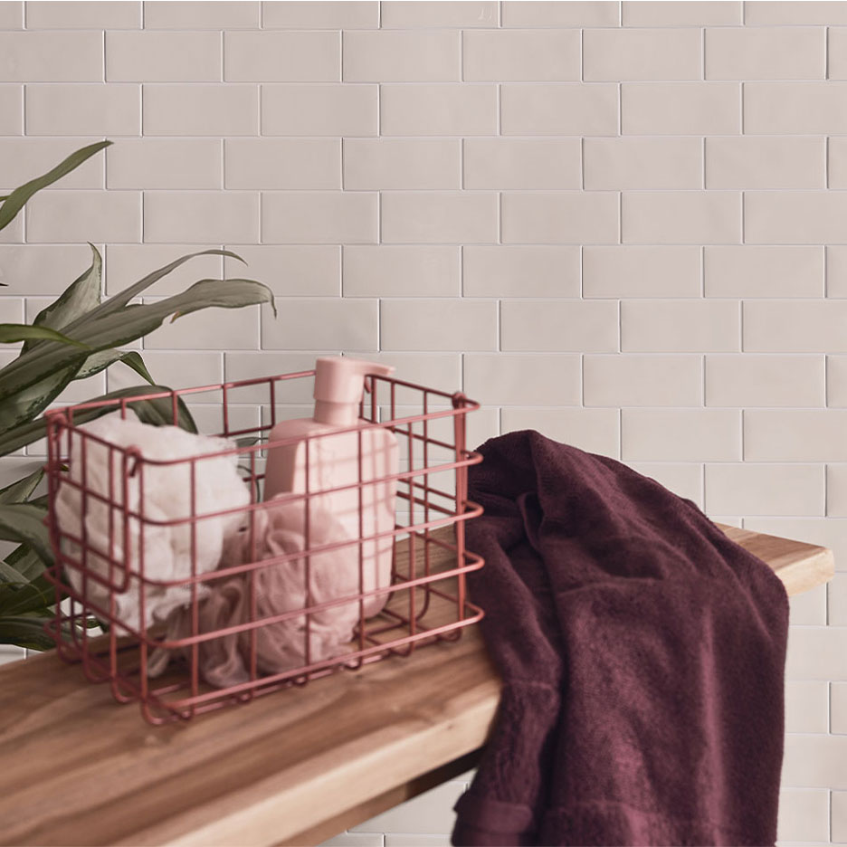 Kylpyhuoneen sisustus valkoisilla laatoilla, puupenkillä, korilla saippualla ja pyyhkeillä.