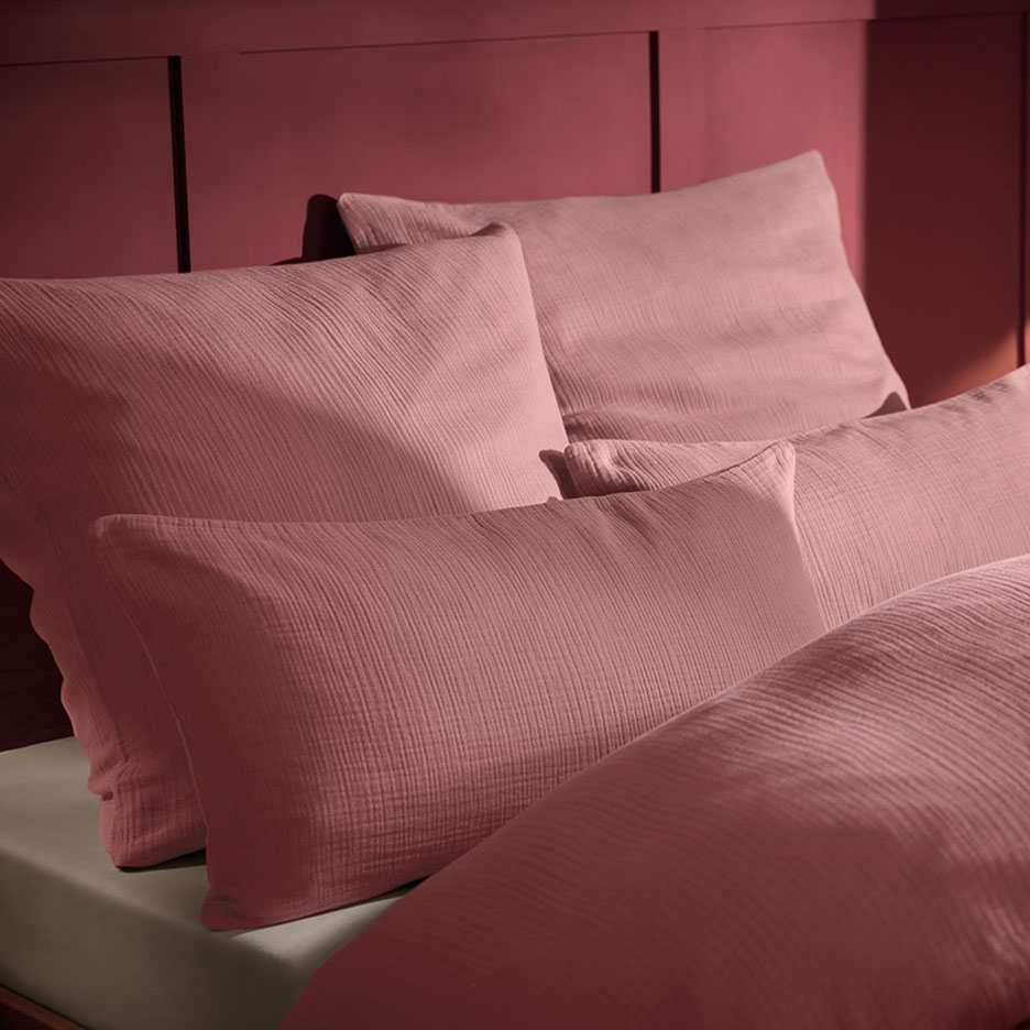 Vaaleanpunainen tyyny ja musliinivuodevaatteet sängyssä, jossa on puinen sängynpääty.