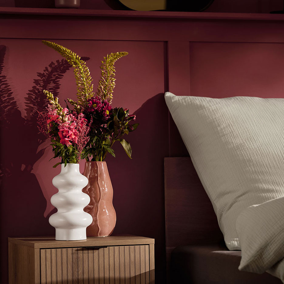 Kaksi maljakkoa kukkia yöpöydällä sängyn vieressä valkoisen tyynyn kanssa.