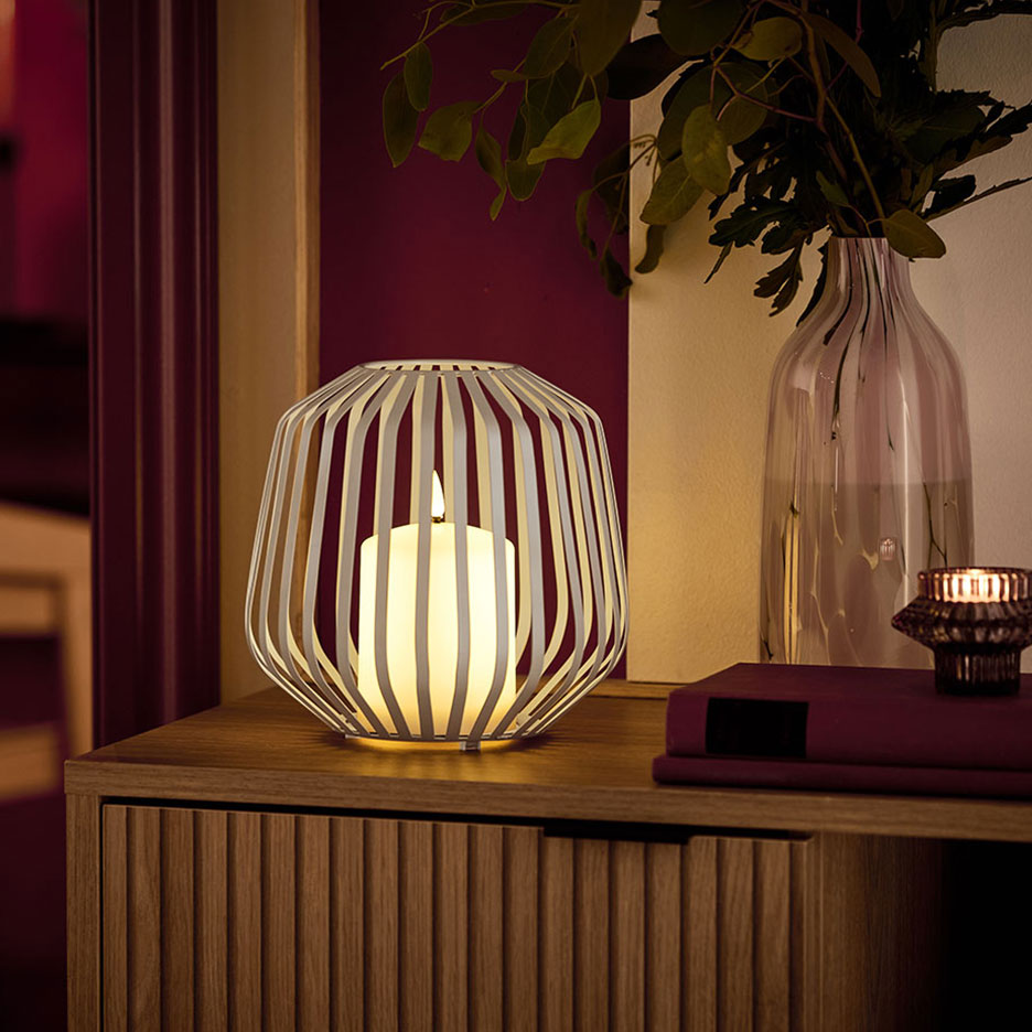 LED-kynttilä valkoisessa metallitelineessä puisen lipaston päällä.