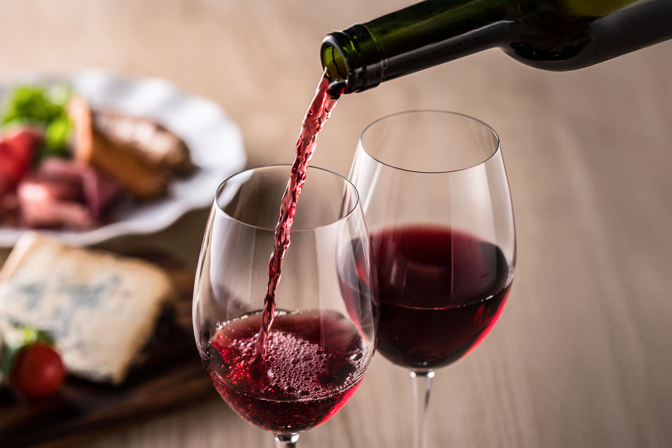 Punaviiniä kaadetaan lasiin, taustalla alkupaloja.