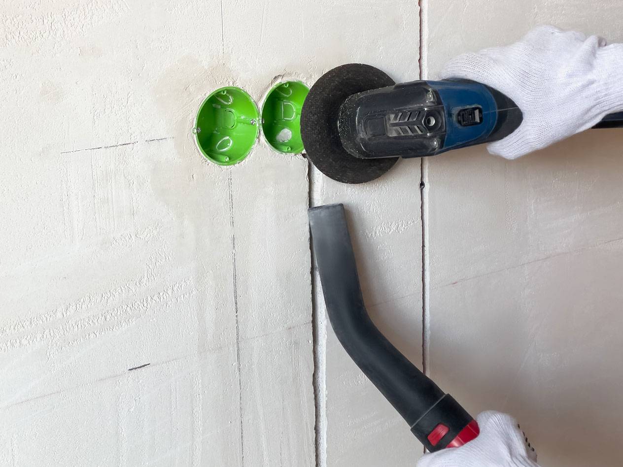 Sähkötyökalu leikkaa uria seinään pölynimurin kanssa pölyä varten.