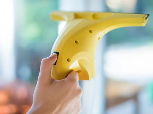 Käsi pitää keltaista sähköistä ikkunanpesuria, puhdistaen ikkunaa.