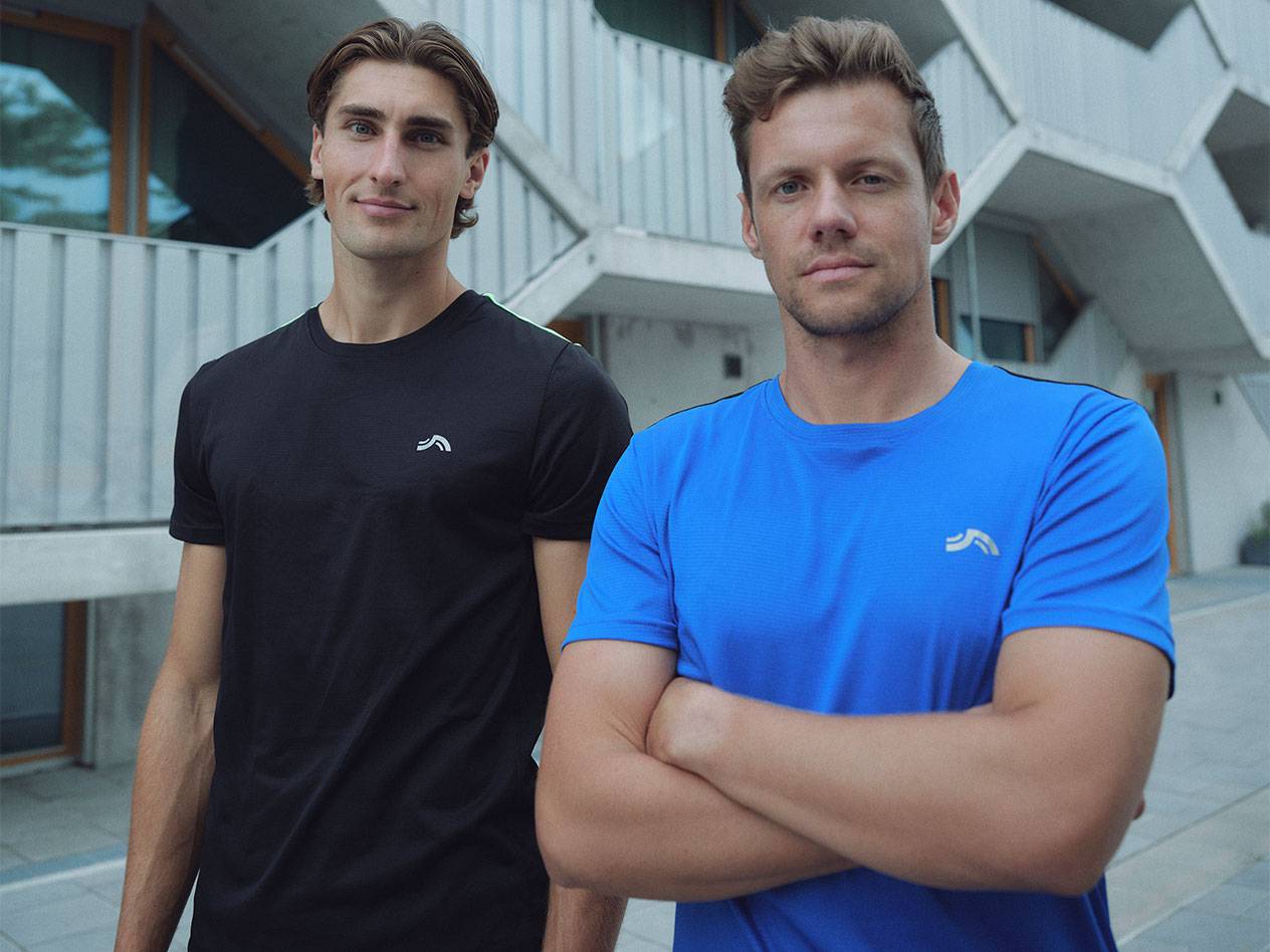 Kaksi miestä mustissa ja sinisissä urheilupaidoissa logolla.