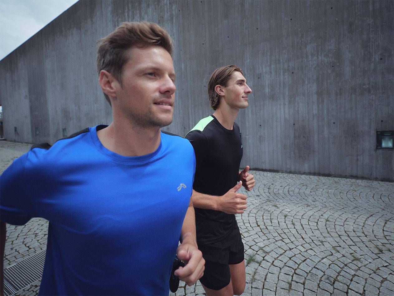 Kaksi miestä juoksee urheilupaidoissa ja shortseissa, toinen sinisessä ja toinen mustassa.