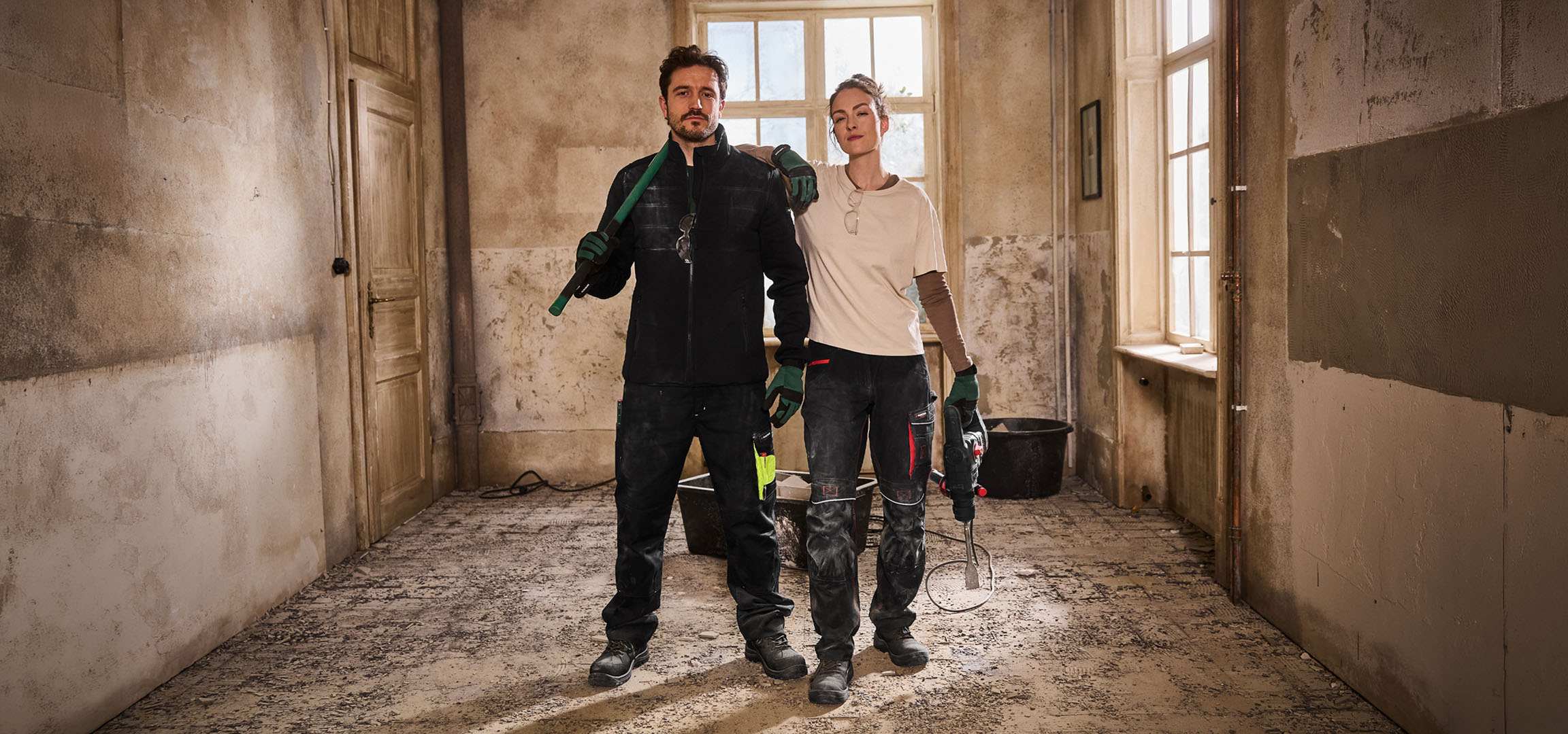 Kaksi rakennustyöntekijää työvaatteissa työkaluineen rakennustyömaalla.