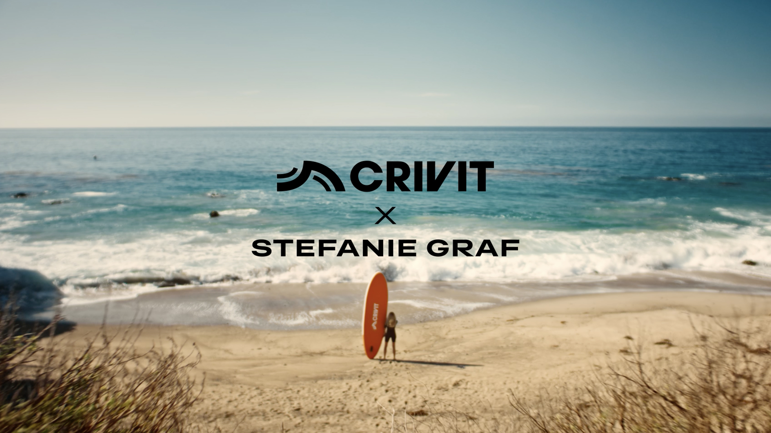 Nainen oranssin SUP-laudan kanssa hiekkarannalla, meri taustalla.