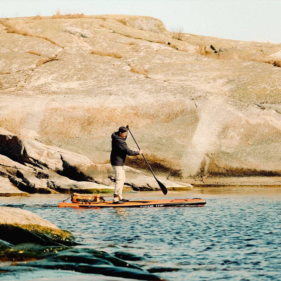 Mies meloo oranssilla SUP-laudalla kivisellä järvellä.
