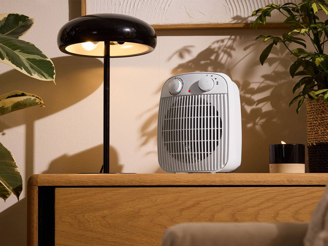 Valkoinen lämmitin ja musta pöytävalaisin puuhuonekalulla viihtyisässä huoneessa.