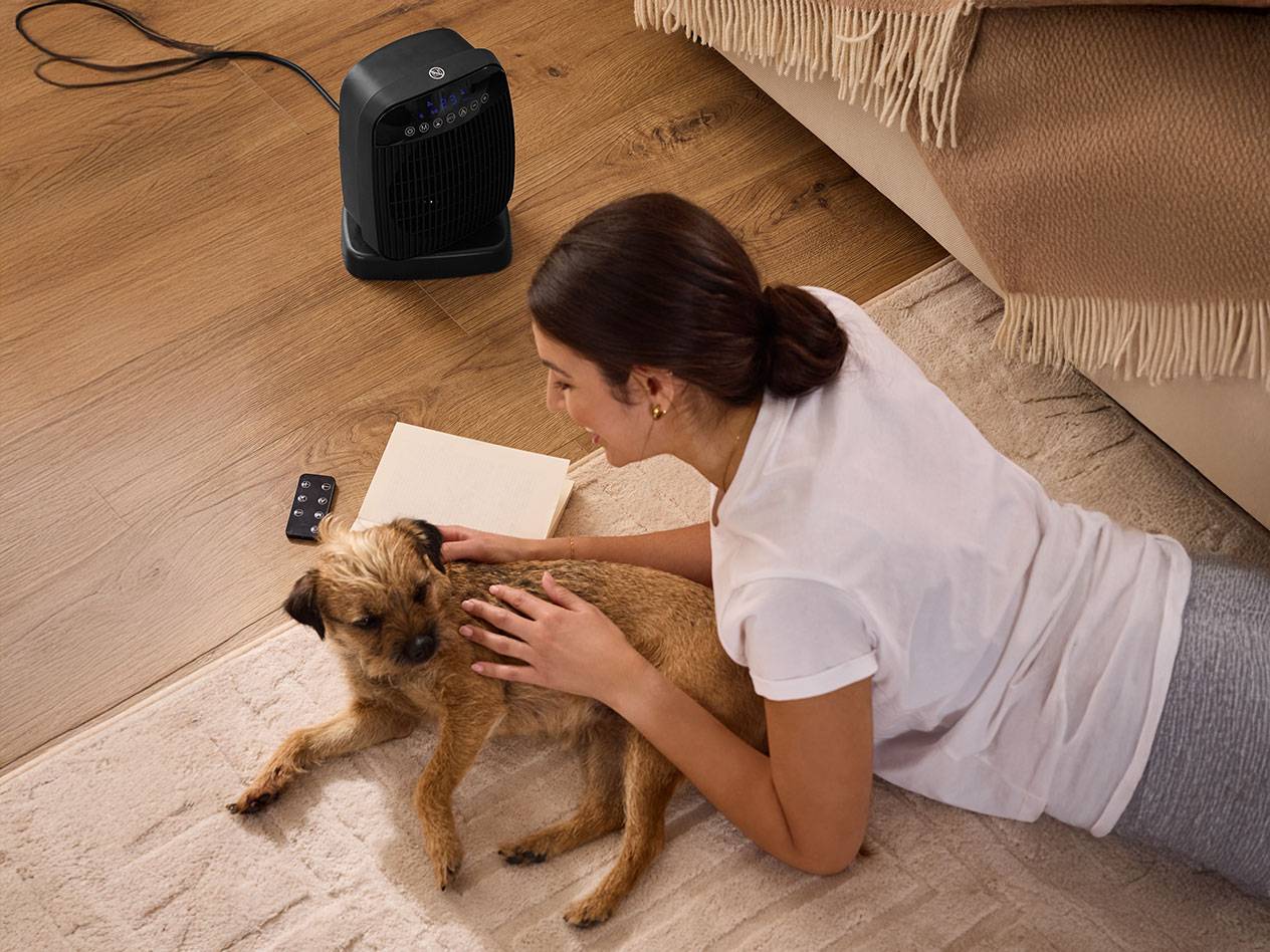 Nainen silittää koiraa mustan tilalämmittimen vieressä lattialla.