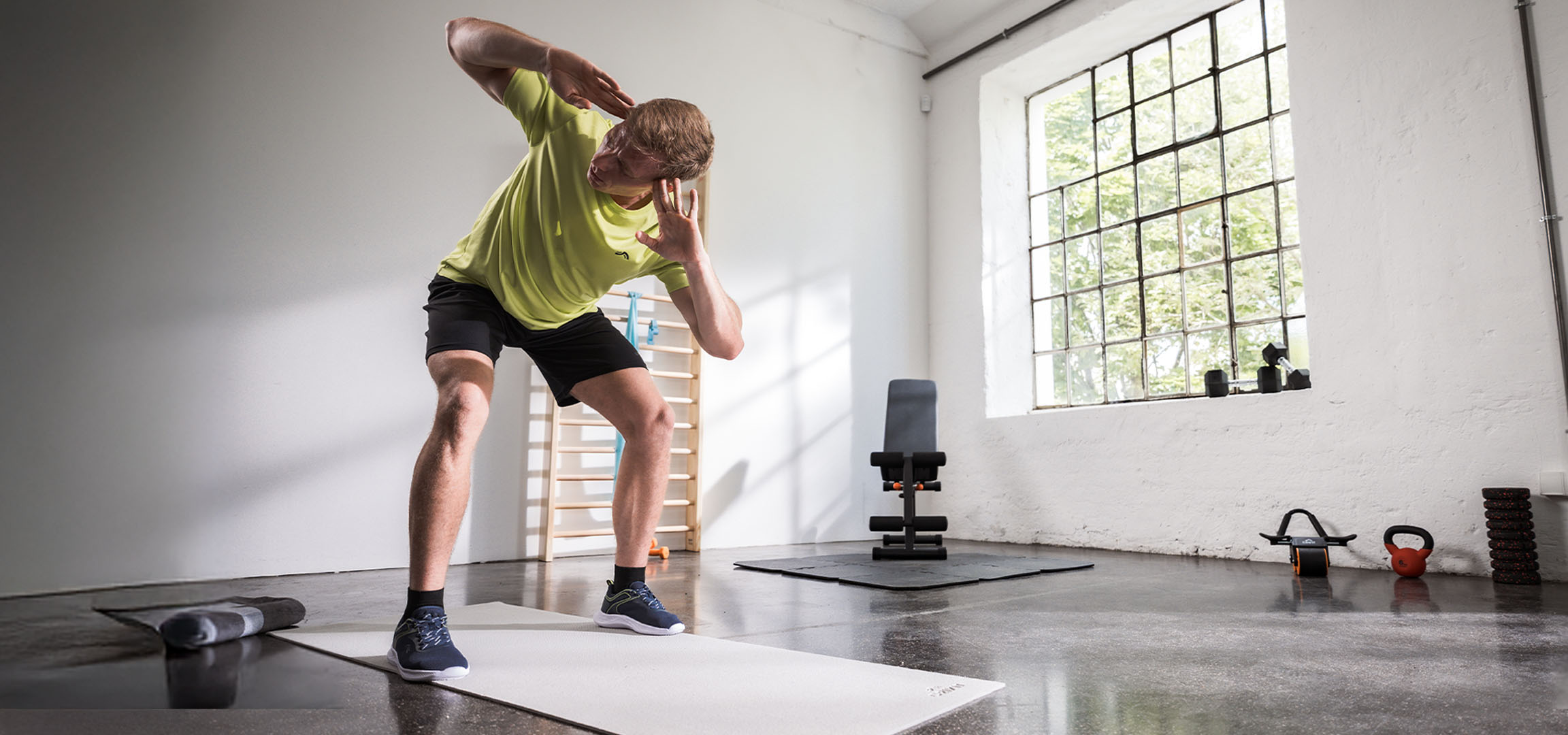 Mies treenaa kuntosalilla joogamaton ja käsipainojen kanssa.