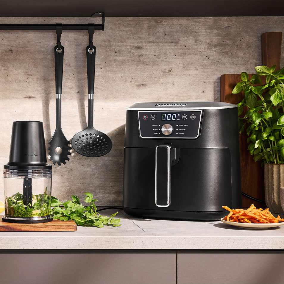 SilverCrest-ilmafriteerauskeitin ja monitoimikone keittiötasolla tuoreiden yrttien ja bataattiranskalaisten kera.