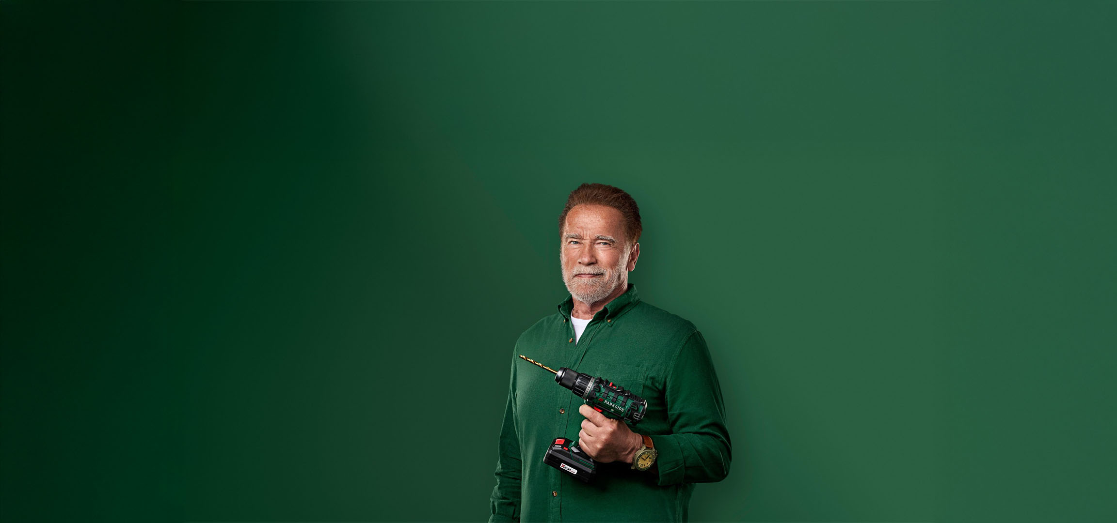 Arnold Schwarzenegger pitää Parkside-porakonetta vihreällä taustalla.