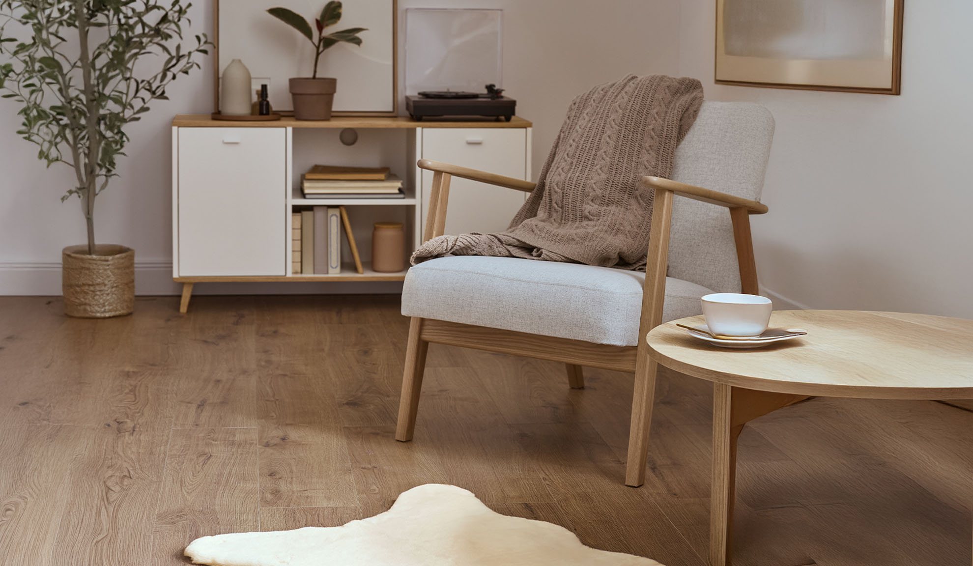 Mukava nojatuoli peitolla, puinen sohvapöytä ja säilytyskaappi valoisassa olohuoneessa.