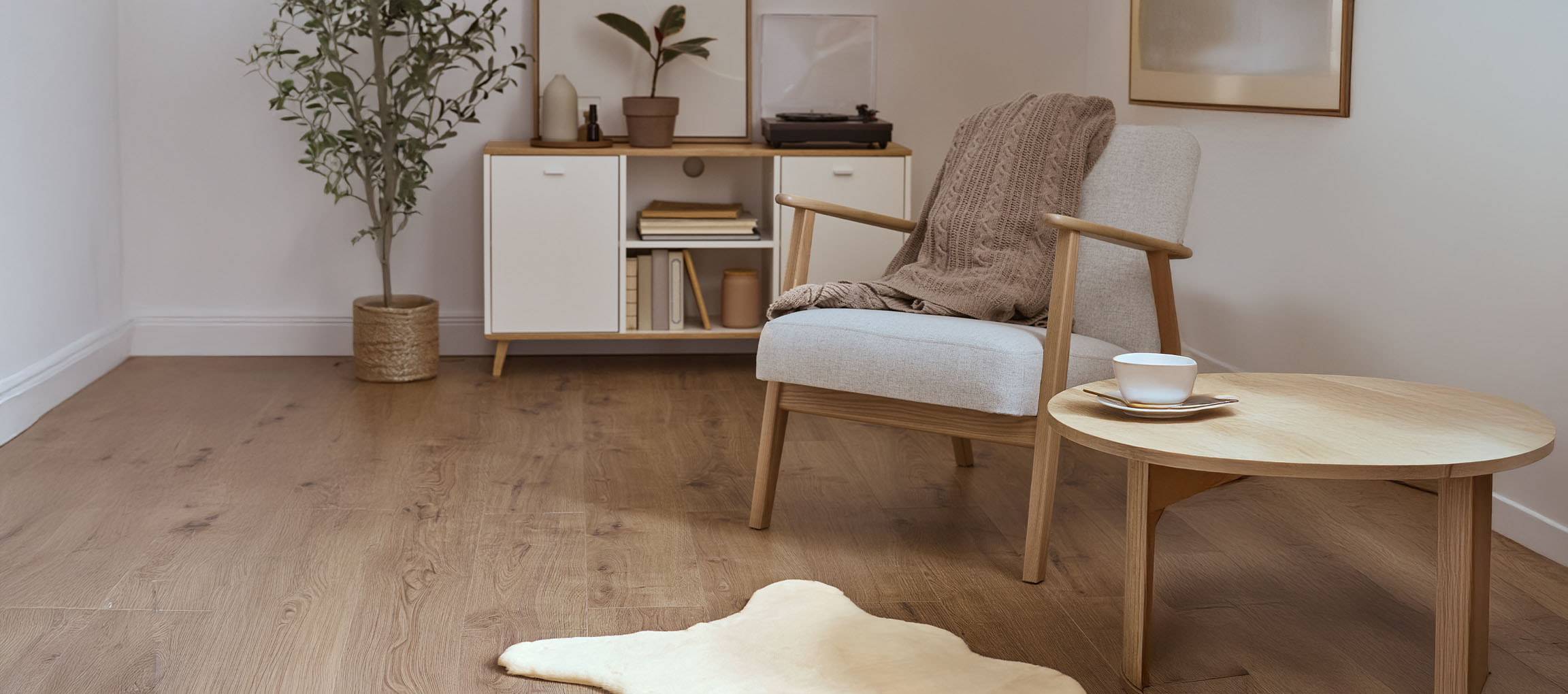 Harmaa kangastuoli neulotulla peitolla, puinen sohvapöytä ja moderni senkki.