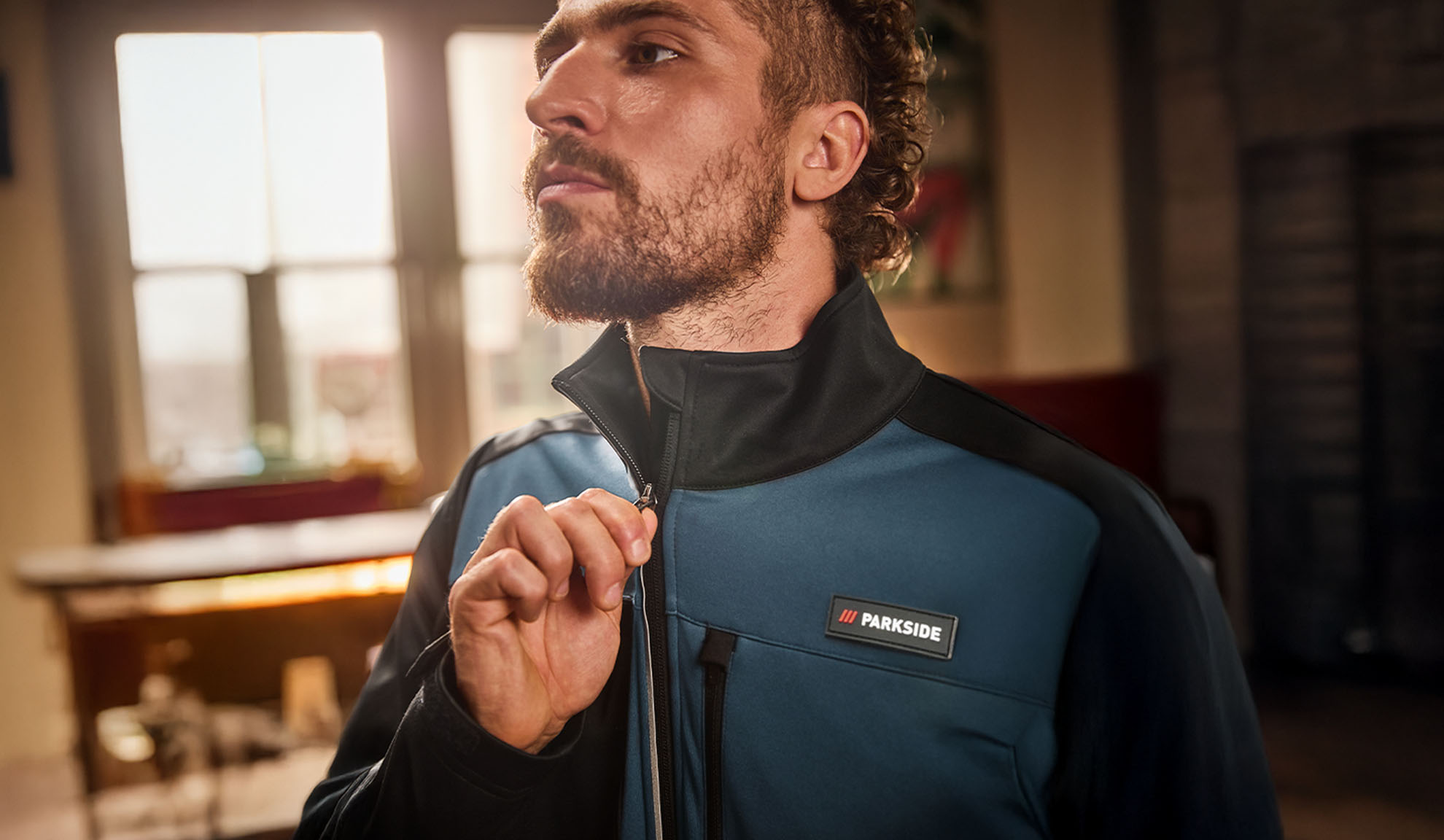 Mies sinimustassa Parkside-työtakissa, vetoketjua sulkemassa.