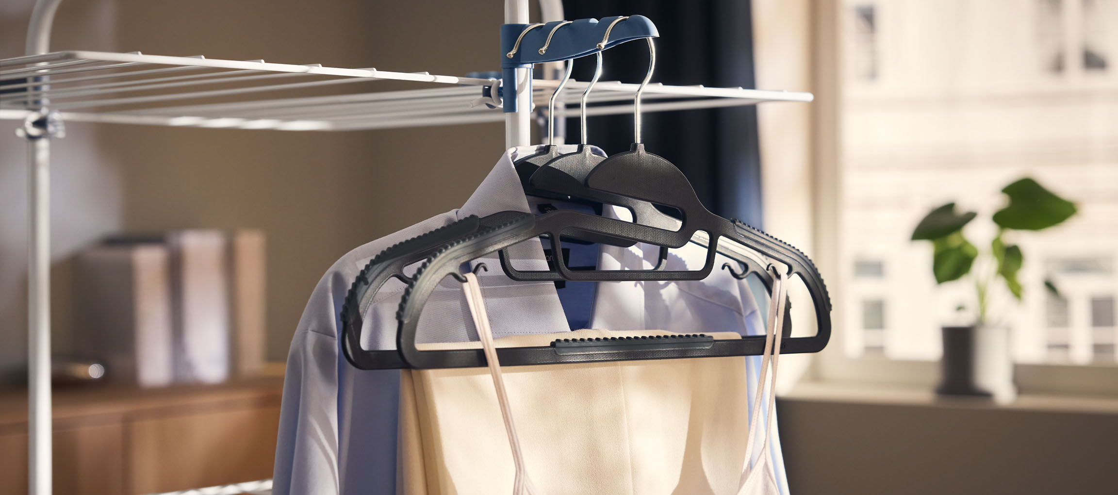 Vaatteita ripustimilla kuivaustelineessä, kasvi taustalla.