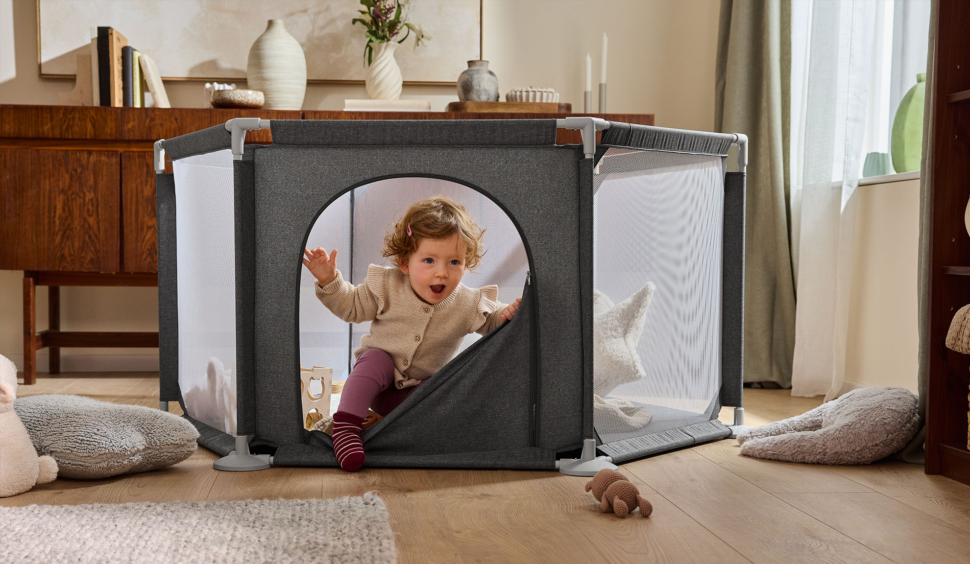 Onnellinen vauva ryömii ulos harmaasta leikkikehästä viihtyisässä olohuoneessa.